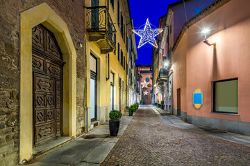 Fototapeta na wymiar Old cobblestone street illuminated with Christmas lights in Alba, Italy.