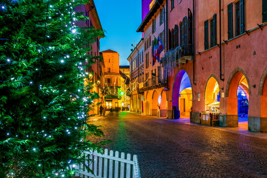 Christmas tree on illuminated cobblestone street in Alba, Italy.