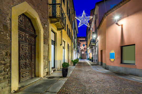 Old cobblestone street illuminated with Christmas lights in Alba, Italy.