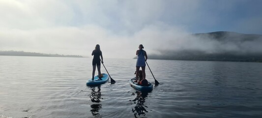 Two young girls on board for Sup surfing raking a wave with  paddle on sunrise.