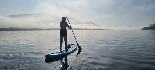 Young girl on board for Sup surfing rakes a wave with paddle on sunrise. Concept of active lifestyle