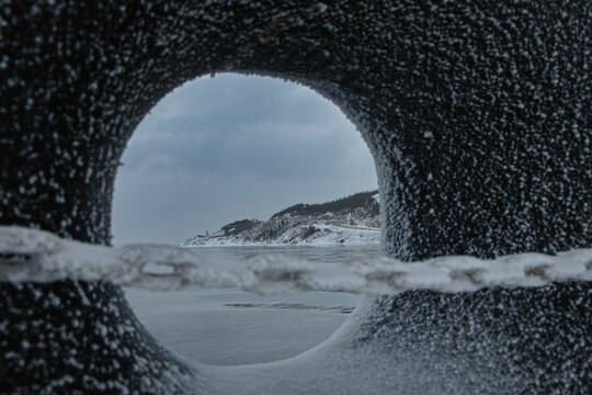 Hole in a snowy stone with mountains and a sandy beach in the background