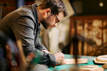Portrait of leather craftsman cuts leather with a scalpel at table in workshop studio