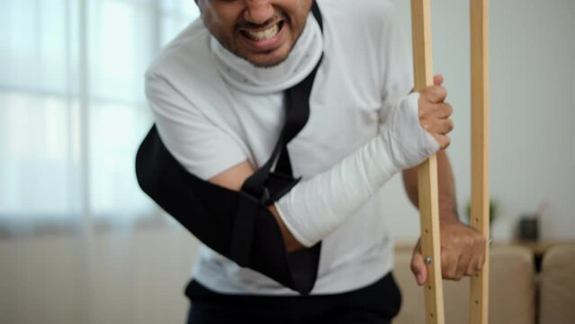 Man suffered pain from accident fracture broken bone injury with leg splints in cast, neck splints collar, sling support arm walking at home with crutch. Social security and health insurance concept.