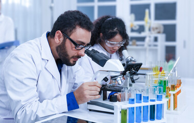 A team of professional male and female scientists working on analyzing samples. Use a microscope and a laboratory lab.