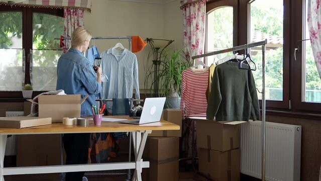 Woman taking pictures of pre-owned clothes for online resale, establishing view.