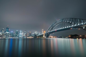 Night shot of Sydney Harbour Bridge and illuminated modern buildings reflected on the water