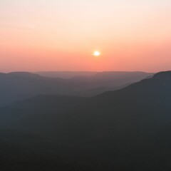 Vertical shot of the setting sun in the distance and fog covering the mountains
