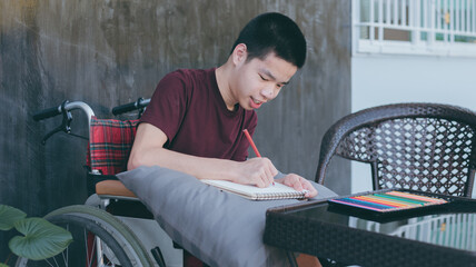 Young man with a disability enjoying training of hand and finger muscles through drawing us pencil...
