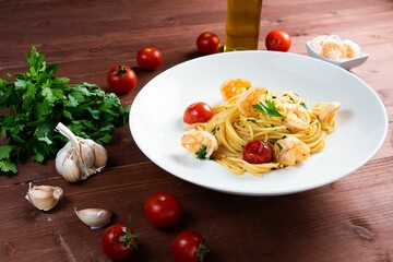 Plate of spaghetti with tomatoes and seafood served on a brown, wooden table and vegetables around
