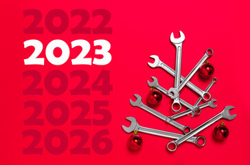 2023 Christmas tree made of wrenches decorated with balls on a red background. Happy New Year...