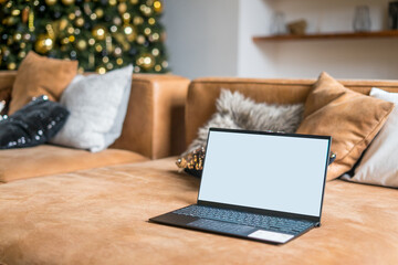 Fototapeta na wymiar Laptop on sofa with isolated white screen for mockup in Christmas time