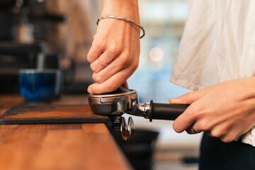 Closeup of barista hands making coffee indoors, wooden board blurred background
