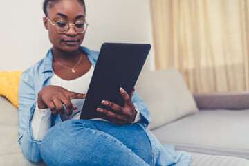 Cropped shot of a beautiful young woman using a digital tablet while relaxing on her sofa at home