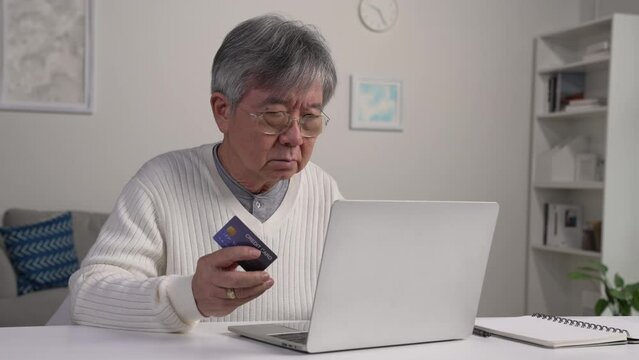 Confused Asian elderly senior retired man, stressed worried sad frustrated male having problem with paying, buying online, payments with credit blocked bank card, laptop. Internet fraud