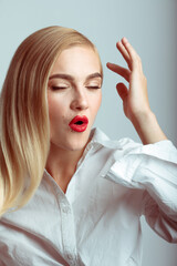 Fashion and make-up concept. Close-up studio portrait of beautiful blonde woman with red lipstick and closed eyes making O shape with lips. Model wearing shirt. Toned image with blue and red color