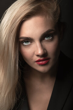 Fashion and business concept. Studio portrait of beautiful blonde woman with long hair, green eyes and red lipstick looking to camera. Model wearing classic black suit. Toned image in beige color