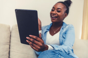 Working from home. A young woman using a digital tablet to read/watch something. Smiling African American woman busy browsing tablet.