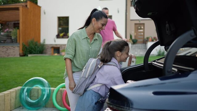 Happy family loading luggage into car before going on summer holiday.