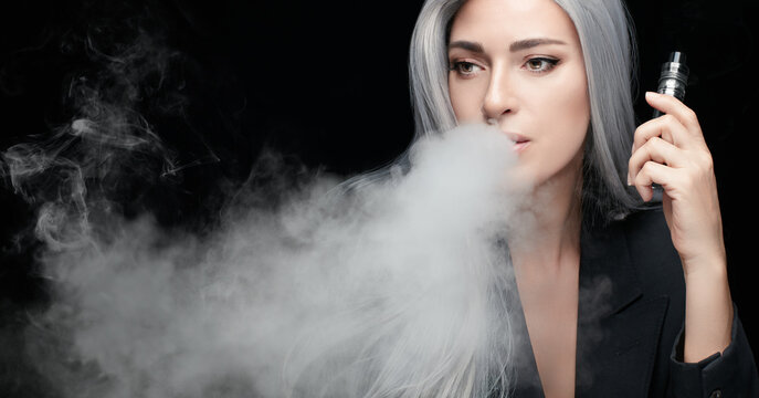 Smoking girl with a vaping device. Silver haired woman blowing a big smoke cloud in a panorama banner isolated on black background with copy space