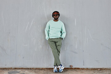 Minimal full length portrait of young black man wearing street style clothes leaning on concrete...