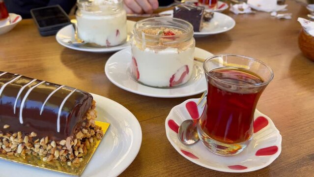Traditional Turkish apple tea glass, chocolate roll with almonds plate and strawberry magnolia yoghurt on table. Sweet dessert sharing concept