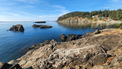 Fototapeta na wymiar Beautiful tranquil sea near the rocky shoreline covered with tall trees on a sunny day