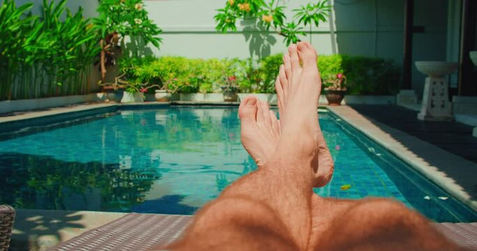 Vacation. Mans feet on the background of the swimming pool, relax on holiday. Brutal male legs with thick dark body hair. Recreation area, sunbed chise-longue.