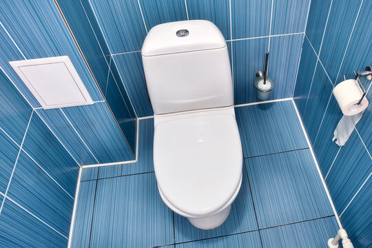white toilet with closed lid in toilet with blue tiled wall. View of clean toilet bowl on top with toilet paper. Room of cramped restroom.