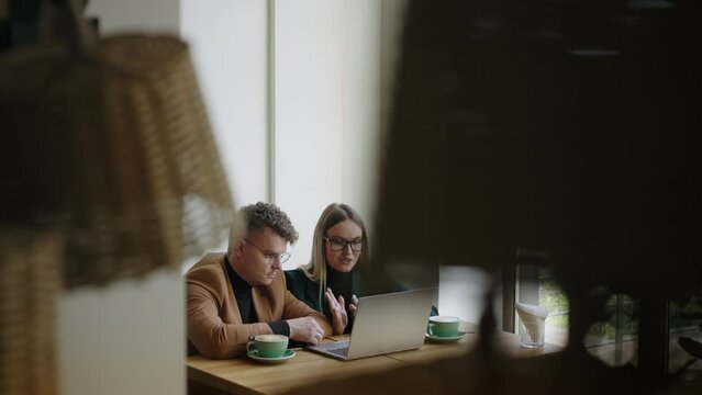 two freelancer meet and working in coffee shop, looking at screen of laptop and drinking coffee