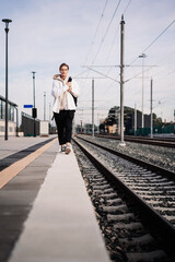 Woman wearing casual white clothes walking on railroad station platform with backpack.