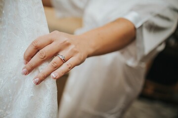 Selective focus of a bride's hand with a promise ring holding her white wedding dress