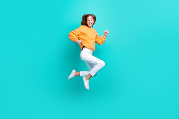 Fototapeta na wymiar Full length photo of cute excited schoolgirl wear orange sweatshirt running fast jumping high isolated turquoise color background