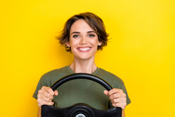 Photo of nice adorable pretty cheeful girl with bob hairstyle wear khaki t-shirt hold steering wheel isolated on yellow color background