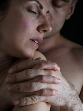 A man hugs a woman from behind. Naked bodies. Plexus of the hands. Close-up photo on a dark background.