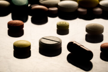 Obraz na płótnie Canvas Differents pills, tablets and capsules scattered on glossy reflective surface with dark shadow. Close up of white, yellow, brown and green medicines. Antibiotics, vitamins, painkillers.