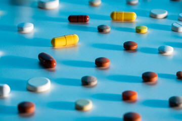 Pattern background from medical tablets, pills and capsules scattered on a blue background. Close up of white, yellow, brown and green medicines. Antibiotics, vitamins, painkillers.