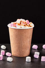 Paper cup with hot drink with marshmallows on dark background.