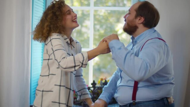 Young pretty girlfriend and overweight boyfriend dance together at home. Realtime