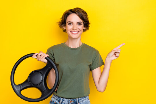 Photo of positive cheerful woman dressed khaki t-shirt hold steering wheel directing empty space isolated on yellow color background