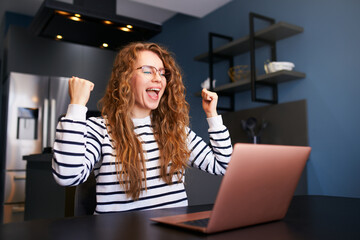 Happy woman checks e-mail, good news about success on laptop. Female rejoice, celebrate visa...