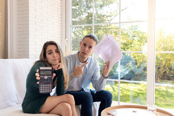 Sad couple with financial problems and troubles showing the calculator and paperwork to the camera after home budgeting