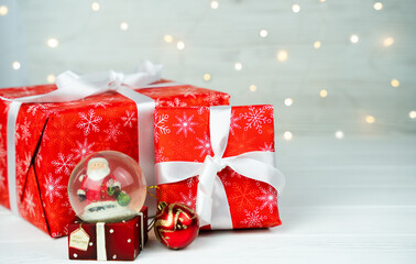 Christmas red gift boxes and Christmas snow globe on the white wooden background. Close-up. Gifts for the New Year and Christmas. Copy space. Selective focus.