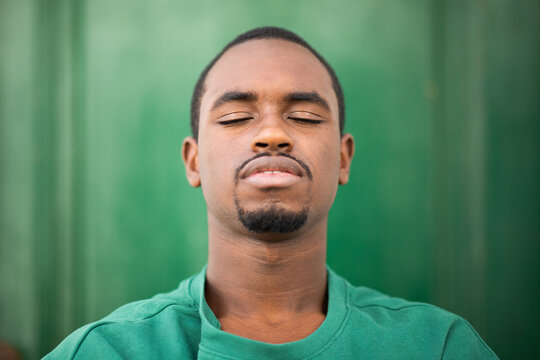 Handsome young african man with eyes closed against green background