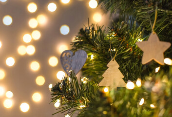 Christmas tree decorated with handmade wooden toys in the shape of a star and heart on a blurry, sparkling background, close-up