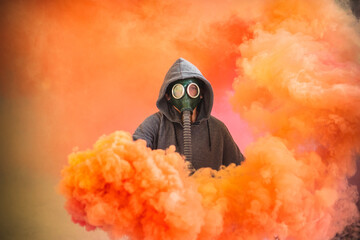 Hooded man wearing a gas mask and holding a smoke bomb surrounded by red and orange smoke