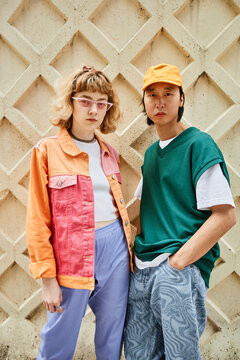 Vertical portrait of two young people wearing colorful street style fashion posing against textured wall outdoors