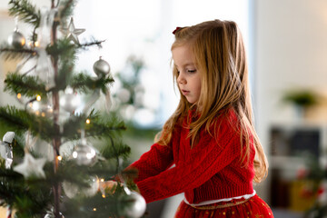 Portrait of a cute little girl decorating a Christmas tree at home for a winter holidays