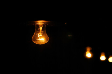 Electric light bulb shines dimly in the dark.