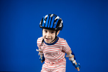 A happy boy in a protective helmet, elbow pads and gloves on a blue background. Protection when...